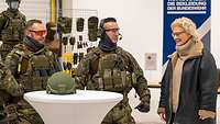 Die Verteidigungsministerin steht mit zwei Soldaten an einem weißen runden Tisch. Auf dem Tisch liegt ein Helm.