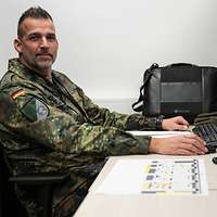 Seitenansicht eines Soldaten im Feldanzug, der an einem Schreibtisch vor einem Rechner sitzt. 