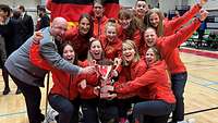 Jubelnde Spielerinnen und ihr Trainer zusammen mit dem Pokal. 