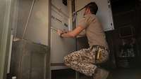Ein Soldat kniet in einem Container zur Stromerzeugung vor der Steuerungseinheit
