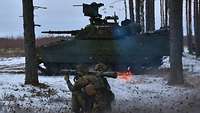 Zwei Grenadiere knien und schießen mit einer Carl Gustaf Waffe, im Hintergrund ist der Schützenpanzer CV90