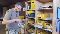 Ein Soldat sortiert in einem Container Briefe in gelbe Plastikkisten