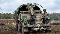 Zwei Soldaten befinden sich auf einem militärischen Schwertransporter auf einem Truppenübungsplatz und verlegen Minen
