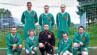 Ein Fußballteam mit acht Spielern in grünen Hemden posiert vor einem Tor für ein Foto. 