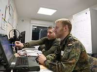 Zwei Soldaten sitzen in einem Container an einem Bildschirm und zeigen auf etwas.