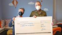 Ein Soldat und eine Frau halten einen überdimensionalen Scheck vor sich.