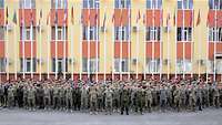 Auf einem Platz vor einem Gebäude mit Flaggen haben sich Soldaten für ein Gruppenfoto versammelt.