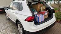 Ein Auto mit offener Kofferraumklappe. Der Kofferraum ist voll beladen mit Weihnachtsgeschenken für Kinder. 