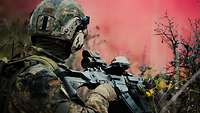 Ein Soldat kniet zwischen Dornenbüschen. Im Hintergrund steigt roter Rauch auf