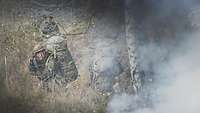 In einer Rauchwolke auf einem Feld sind mehrere Soldaten zu erkennen