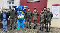 Soldatinnen und Soldaten, sowie ein Mann in ziviler Kleidung stehen vor einer Kinder hospiz.