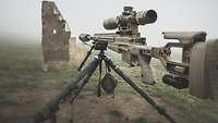 Auf einem Dreibein ist ein Gewehr G22 montiert. Vor der Waffe steht eine Holzdeckung mit einem kleinen Loch 
