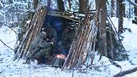 Drei Soldaten sitzen im Shelter an einem Lagerfeuer