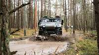 Ein gepanzertes Militärfahrzeug vom Typ Eagle V fährt im Wald durch eine große Pfütze