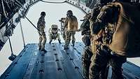 Mehrere Soldaten springen über die geöffnete Heckrampe eines Flugzeuges in den sonnigen Himmel.
