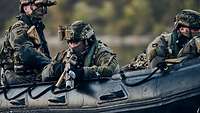 Mehrere Soldaten liegen mit dem Gewehr im Anschlag im schwarzen Schlauchboot auf dem Wasser.