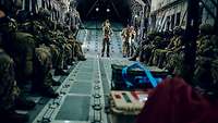 Viele Soldaten sitzen in einem dunklen Flugzeugrumpf in Reihe an den Seiten und warten auf den Sprung.