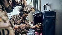 Zwei Soldaten hocken in einer Halle vor einem Koffer und führen eine Kamerasonde ein.