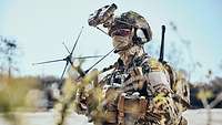 Ein Soldat steht auf einer Sandfläche und hält eine Satellitenantenne in der Hand.