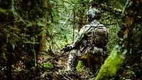 Ein Soldat kniet mit dem Gewehr in einem dichten grünen Wald.