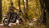 Ein Soldat sitzt auf einem sandfarbenen Motorrad im Wald.
