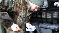 Ein Soldat steht vor dem Dieselgenerator und hat einen Peilstab und ein Papiertuch in der Hand. Er liest den Ölstand ab.
