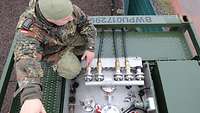 Ein Soldat kniet neben den Anschlüssen der Dieselgeneratoren auf dem Dach des Dieseltanks. 