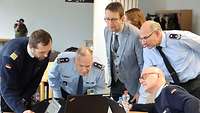 Mehrere Soldaten sitzen am Tisch und schauen auf einen Monitor.