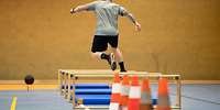 Eine Person springt in einer Sporthalle über mehrere Hindernisse.