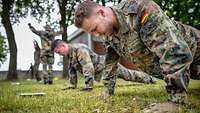 Auf der Wiese eines Sportplatzes machen mehrere Soldaten nebeneinander Liegestütz.