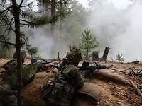 Zwei Soldaten liegen beim Gefechtsschießen mit ihren Maschinengewehren im waldigen Gelände. Rauch liegt in der Luft.