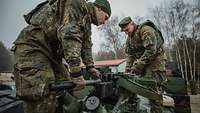 Zwei Soldaten stehen auf einem Militärfahrzeug und hantieren an einer Granatmaschinenwaffe