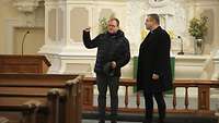 Pfarrer und Bischof stehen vor dem Altar einer evangelischen Kirche.