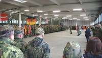 Soldaten und Zivilisten stehen angetreten in einer Halle.