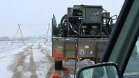 Ein Tankwagen steht auf verschneiter Straße; im Vordergrund ist der Ausschnitt eines Geländewagens zu erkennen