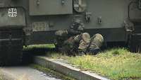 Ein Soldat liegt am Boden hinter einem gepanzerten Fahrzeug