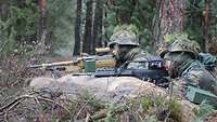 Zwei Soldaten mit Gewehr im Anschlag hinter einem Schutzwall im Wald
