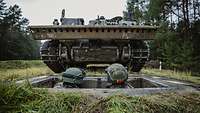 Panzerüberrollbahn Zwei Solaten schauen aus einem Bodenloch, während ein Bergepanzer auf sie zurollt