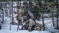 Drei Soldaten knien im Wald und bauen ihr Arbeitsgerät im Schnee auf