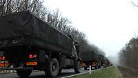 Mehrere Militärfahrzeuge fahren eine Straße mit dichten Nebel entlang.