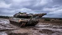 Ein Panzer fährt über eine braune matschige Straße auf einem Feld.