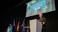 Soldat steht am Rednerpult, hinter ihm eine Projektion mit der Aufschrift Cyber- und Informationsraum: der Bestpreis 2022.