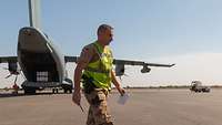 Ein deutscher Soldat mit Warnweste läuft auf dem Vorfeld des Flughafens Bamako entlang, hinter ihm ein Transportflugzeug