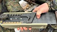 Soldaten stehen hinter einer Haubitze und halten ein technisches Gerät aus Metall in ihrer Hand. 