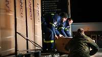 Drei Männer verladen nachts Güter aus Lkw.