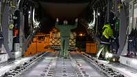 Ein Soldat steht im Laderaum eines A400M und weist einen Gabelstapler voll mit Hilfsgütern ein.
