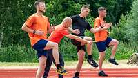 Ein Trainer mit drei Sportlern beim Erläutern und Trainieren einer Lauftechnik.