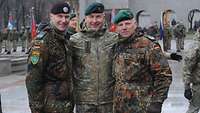 Drei Stabsoffiziere stehen nebeneinander. Im Hintergrund stehen angetretene Soldaten. 