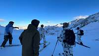 Eine Gruppe von fünf Soldatinnen und Soldaten auf Skiern schauen ins Tal, um sich den Weg für die Abfahrt einzuprägen.