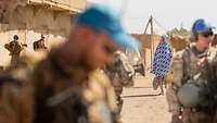 Eine Frau in blau-weißem Gewand läuft an Soldaten vorbei, die im Vordergrund stehen